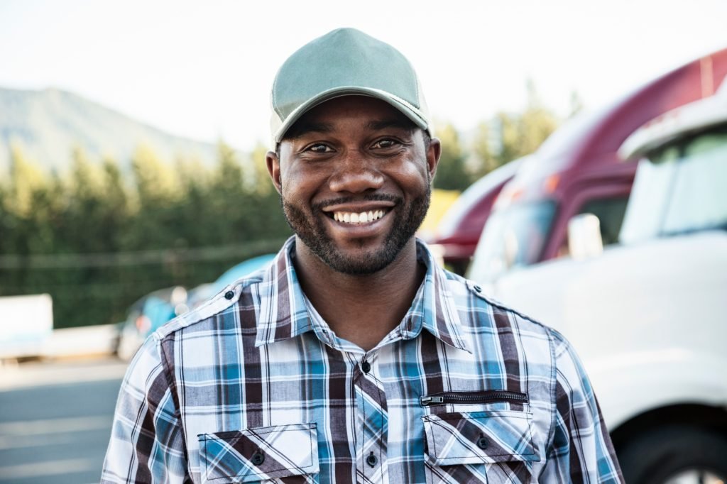 Black man truck driver near his truck parked in a parking lot at a truck stop