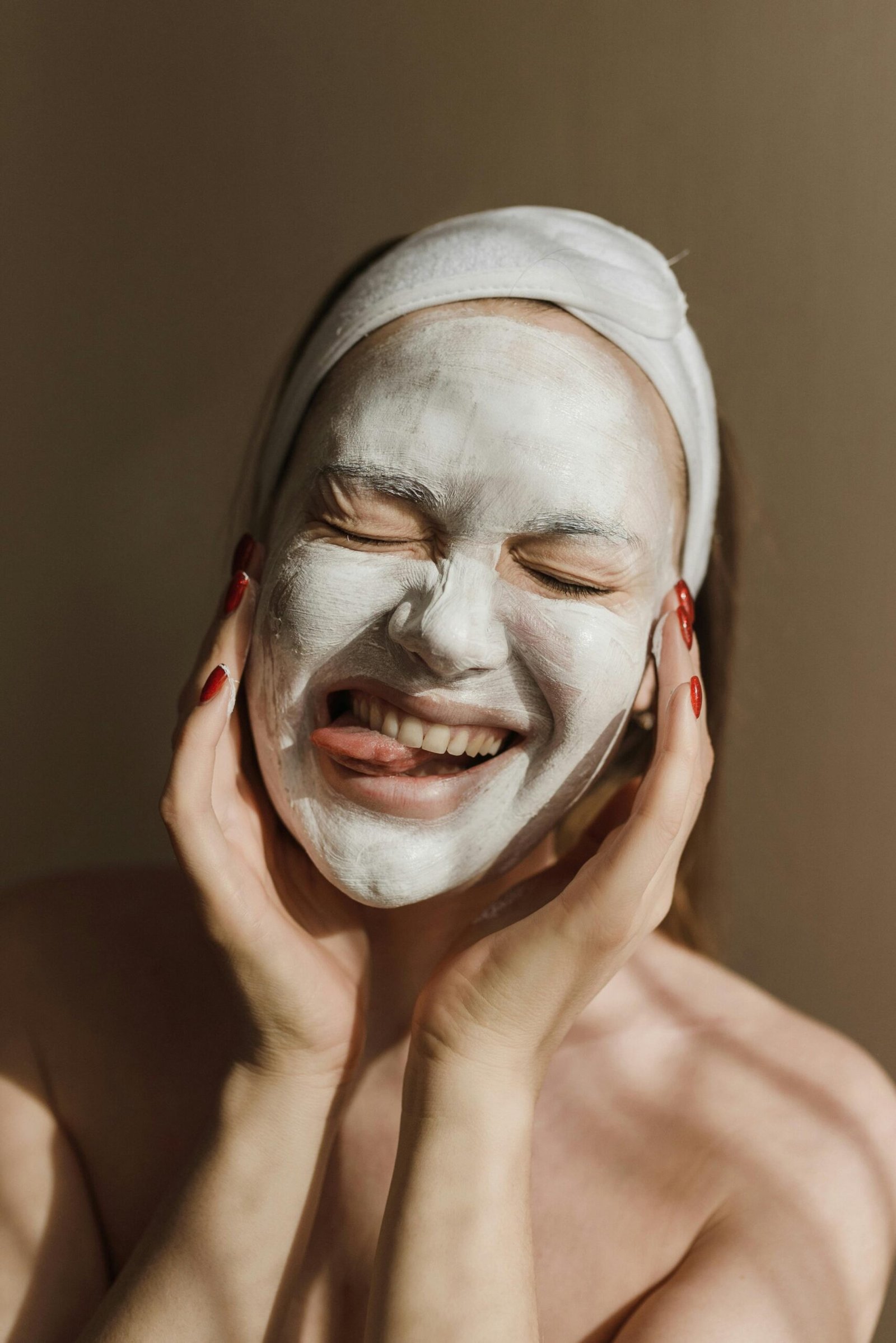 A person with a white face mask and headband smiles with eyes closed, hands on cheeks, conveying a joyful and relaxing moment.